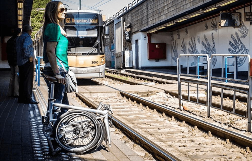 STOP CARS 4 MILLION IN CYCLE LANES woman waiting for the train with her folding ahooga folded for effortless multiple mobility.